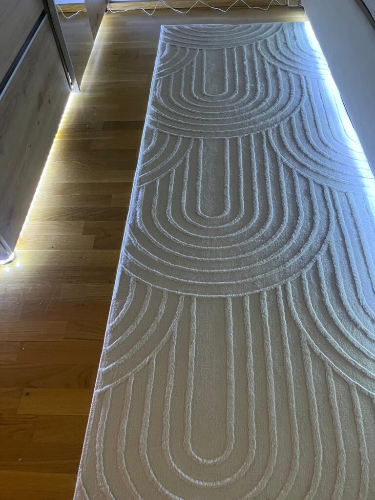Beige SIMPEX boho rug with 3D geometric design placed in a hallway with wooden flooring and LED lighting.