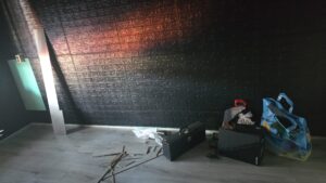 Unfinished black bedroom wall with renovation tools, loose flooring planks, and construction materials in a gemeente apartment in the Netherlands.