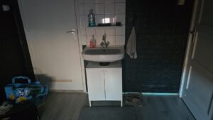 Small wall-mounted sink with a white cabinet installed inside a bedroom due to lack of space in the bathroom and toilet of a gemeente woning in the Netherlands.