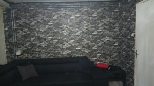 Black L-shaped sofa against a dark stone-patterned wallpaper in the livingroom before redecoration.
